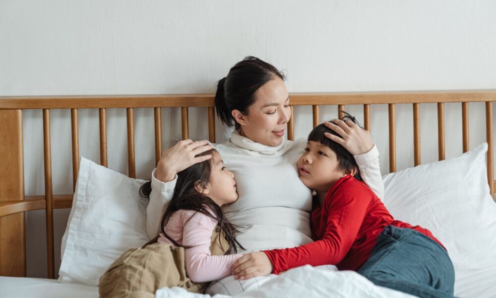 媽媽靠在床頭，一手摸著女兒、一手摸著兒子的頭，三人相視微笑