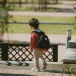 穿紅色外套、背著黑色小背包的幼兒，走在公園步道上的背影