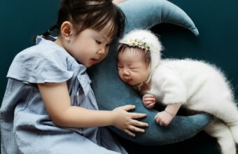 綁著馬尾的小女孩輕輕摸著躺在月亮造型抱枕上熟睡的新生兒
