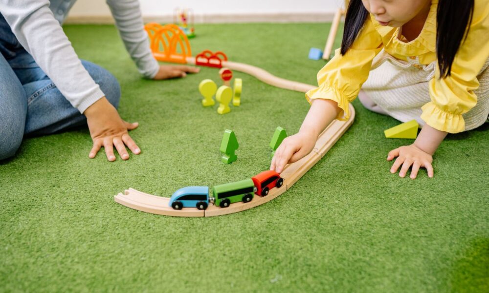 小女孩在綠色地墊上推著木頭小火車軌道玩具