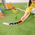 小女孩在綠色地墊上推著木頭小火車軌道玩具